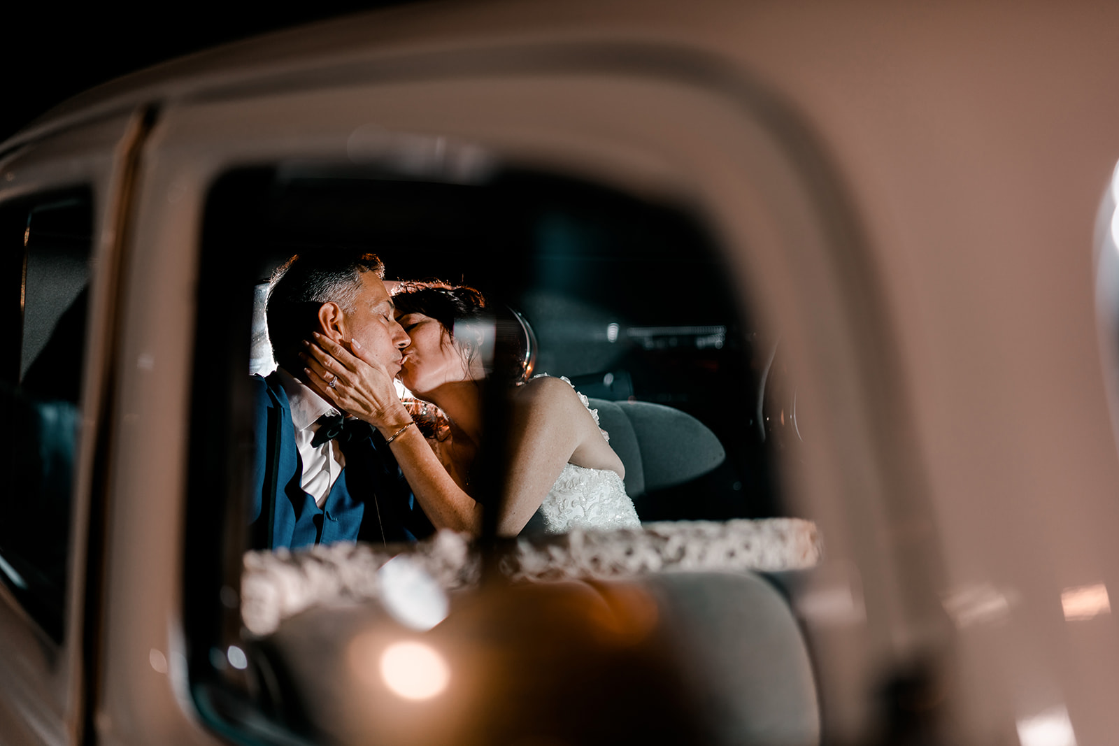 A bride and groom share a kiss inside a car at night, viewed through the car window—an intimate moment beautifully captured by a luxury wedding photographer los angeles.