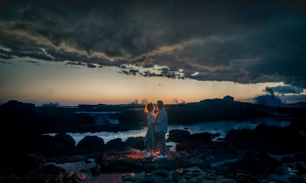 A wedding couple standing on rocks in front of a stormy sky.