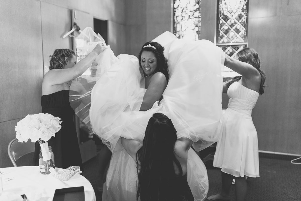 Photographer Thomas Kim captures the bride being helped into her wedding dress by her bridesmaids.