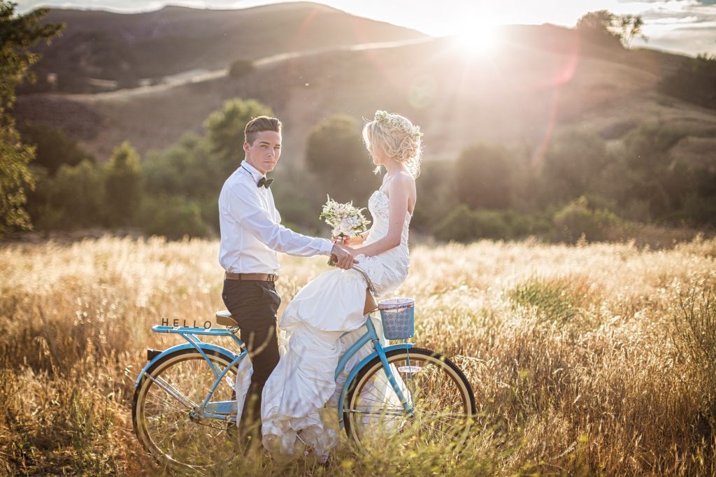 A wedding couple posing next to a blue bicycle in a field.