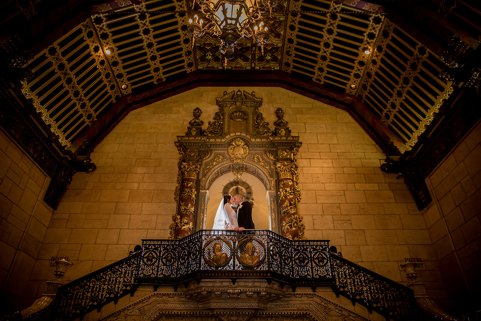 A bride and groom posing for a wedding photographer on the stairs of an ornate building in Los Angeles.
