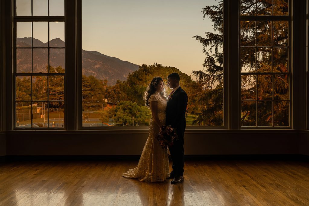 A bride and groom photographed by Thomas Kim in front of a window with mountains in the background.