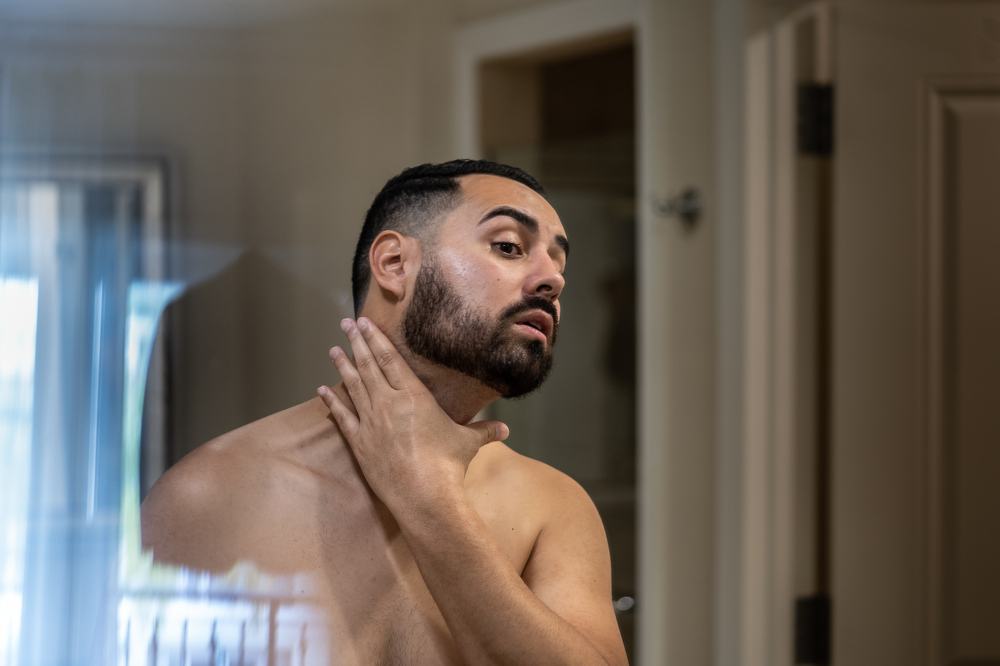 ThomasKim_photography A man is grooming his beard in front of a mirror.