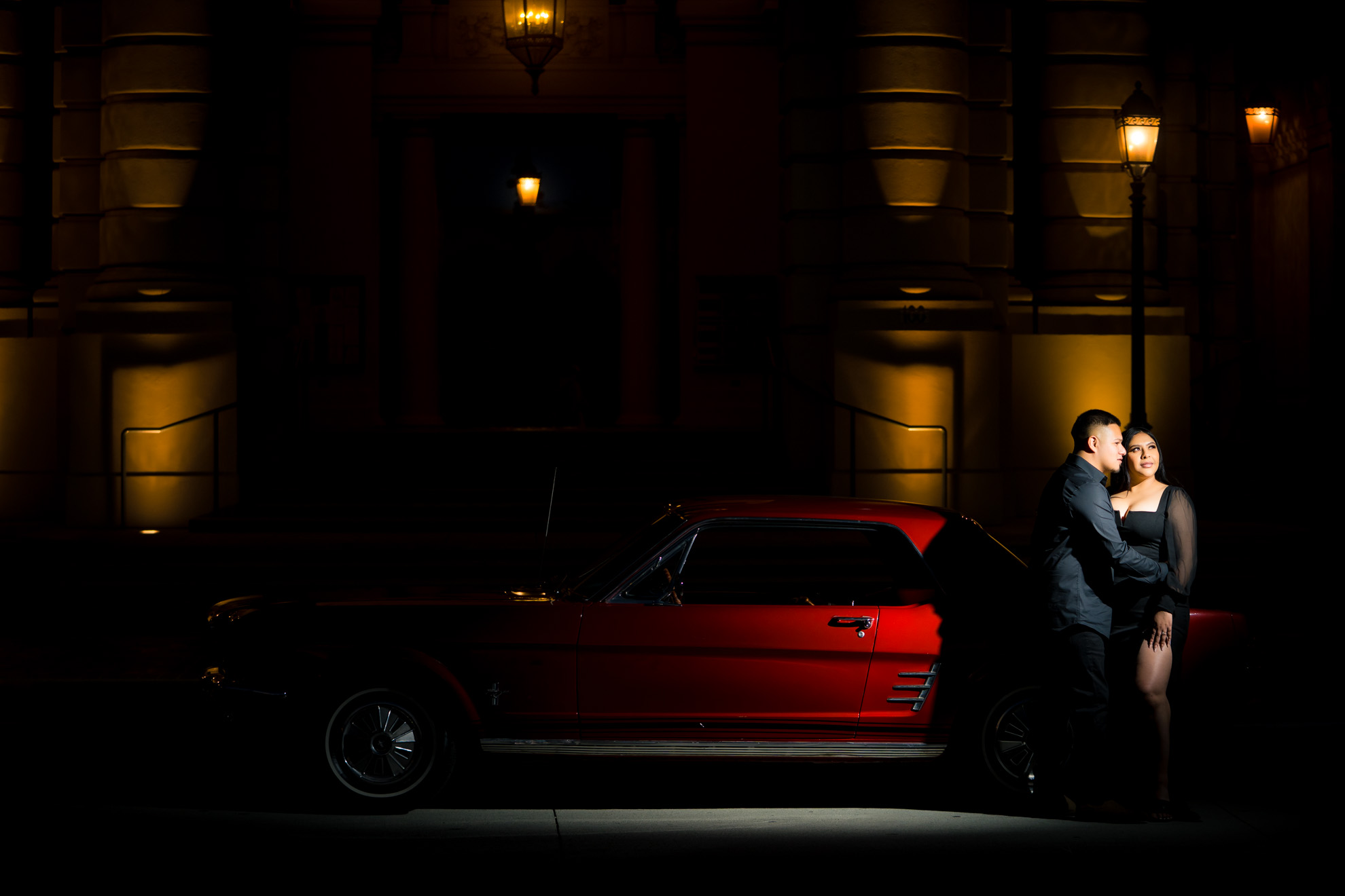 ThomasKim_photography A couple posing in front of a red car at night.
