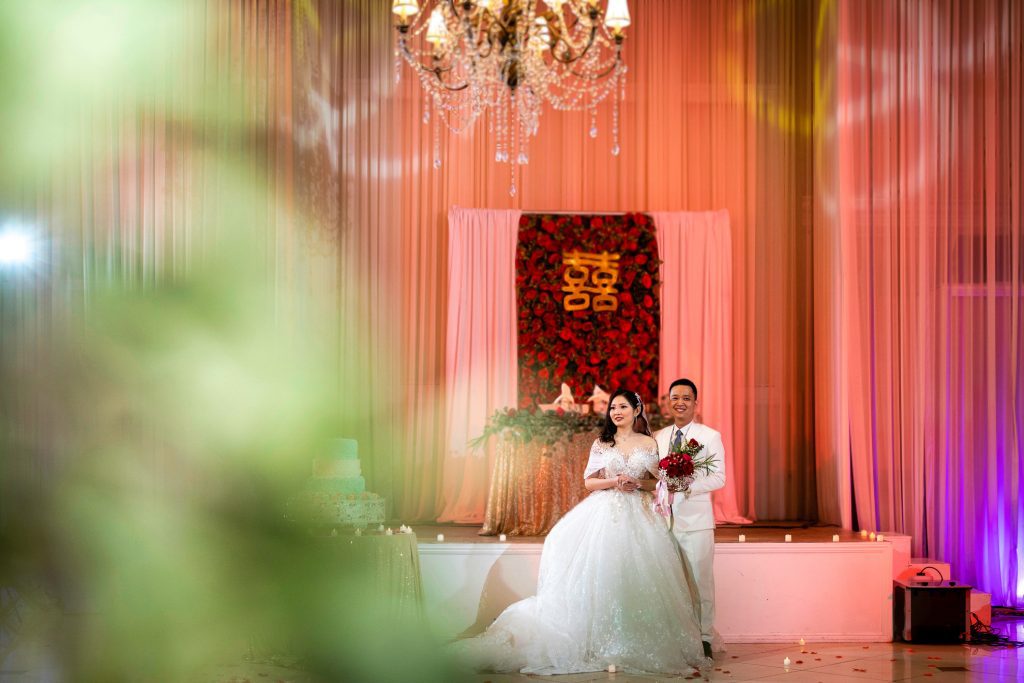 ThomasKim_photography A bride and groom standing in front of a chandelier, emphasizing the elegance.