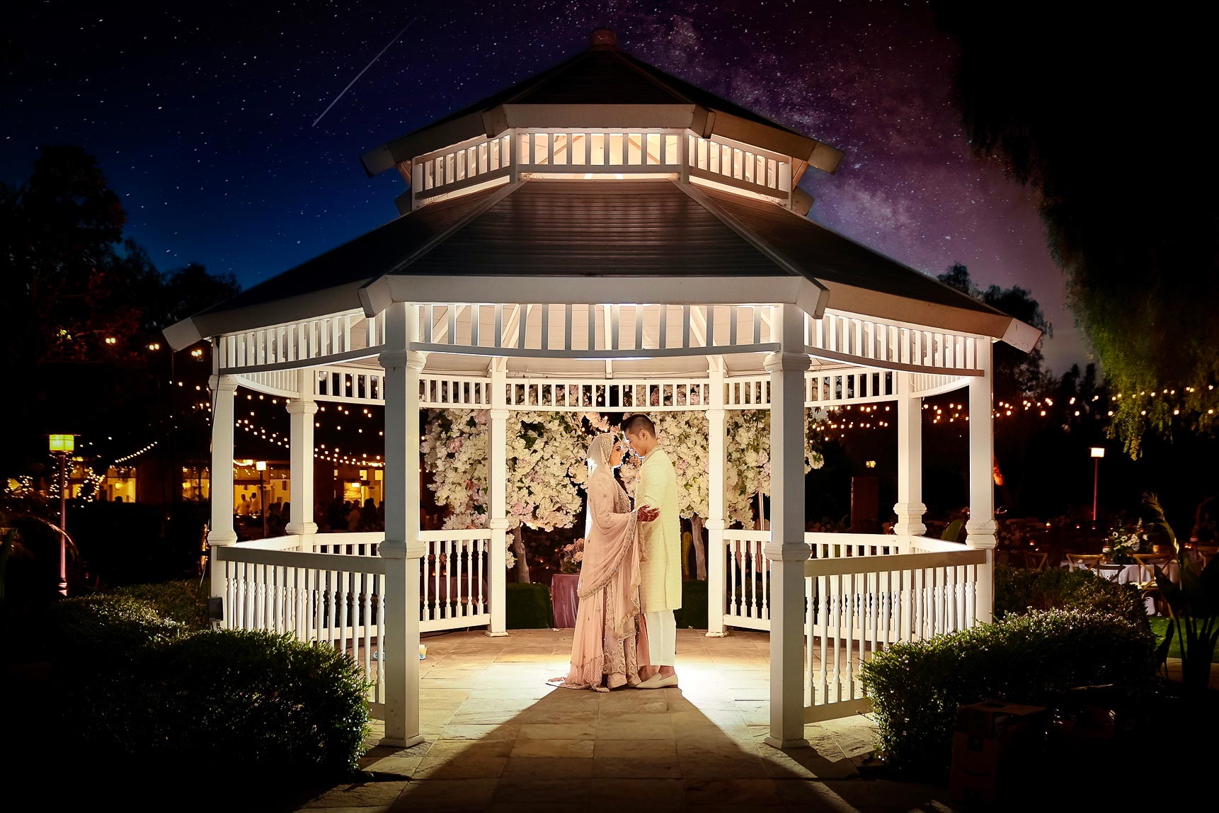ThomasKim_photography A bride and groom standing under a gazebo at night.