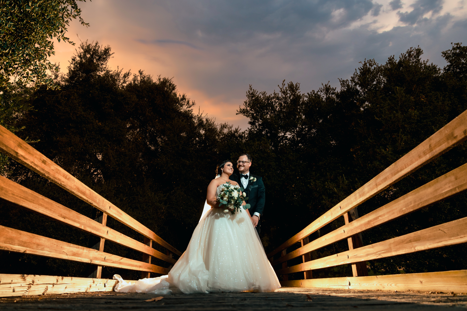 ThomasKim_photography J & M, a bride and groom, standing on a bridge at sunset.