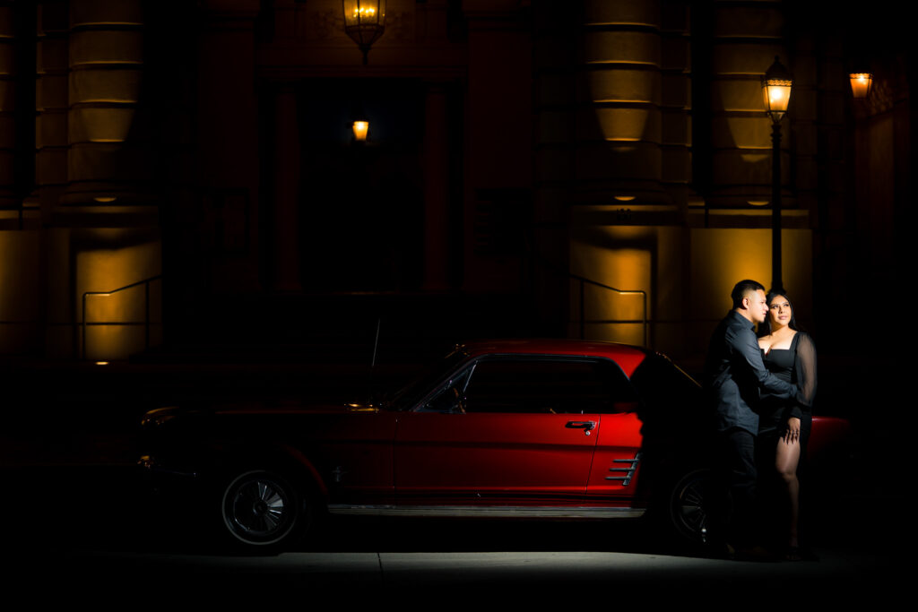 ThomasKim_photography A couple posing in front of a red car at night.