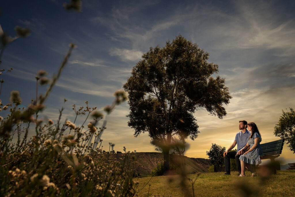 ThomasKim Photography Los Angeles Wedding Photographer A couple sits together on a bench in a grassy field at sunset