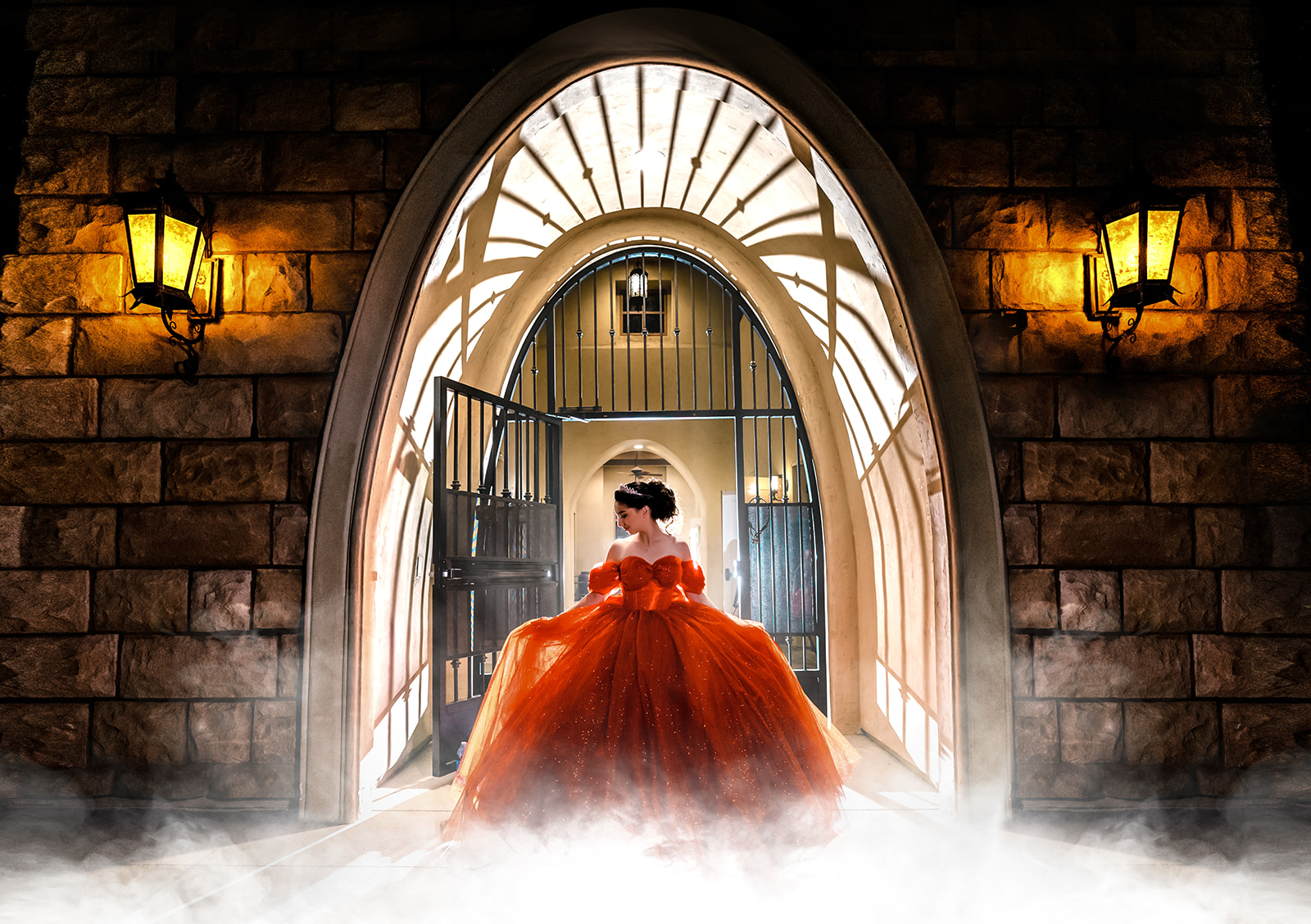 A person in an orange gown stands in an arched stone doorway, with dramatic lighting, open gates behind them, and lamps on the wall. Mist covers the ground in the foreground.
